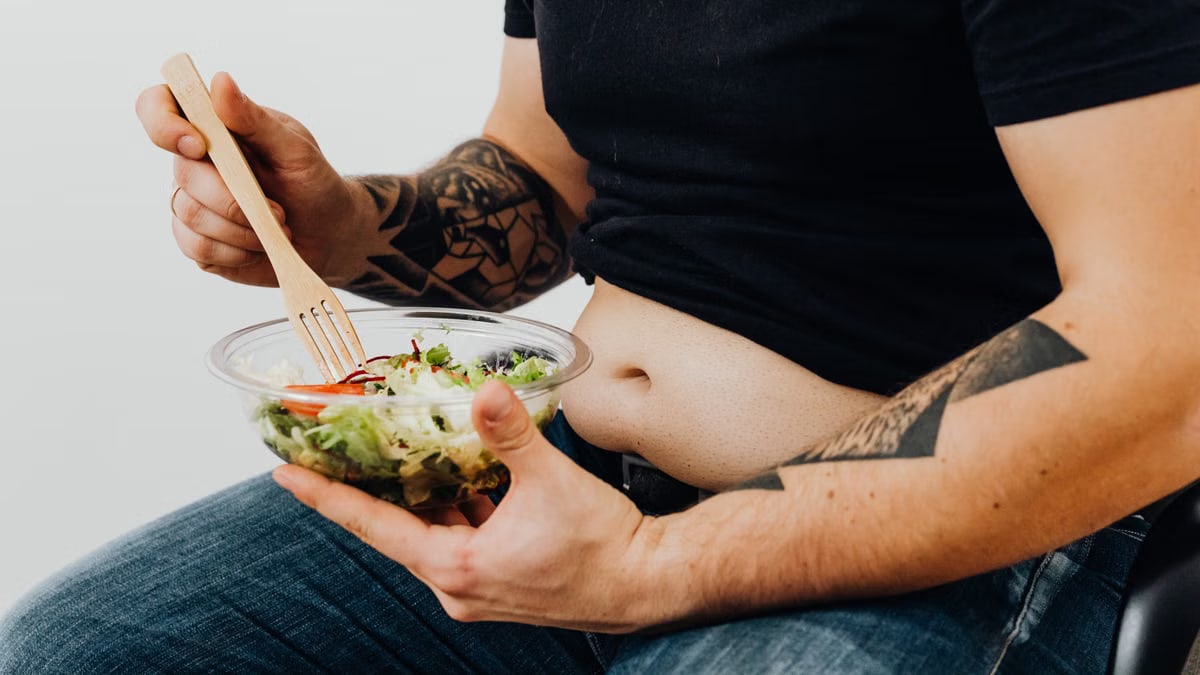 A tattooed individual holding a fresh salad, symbolizing healthy lifestyle and fitness motivation.