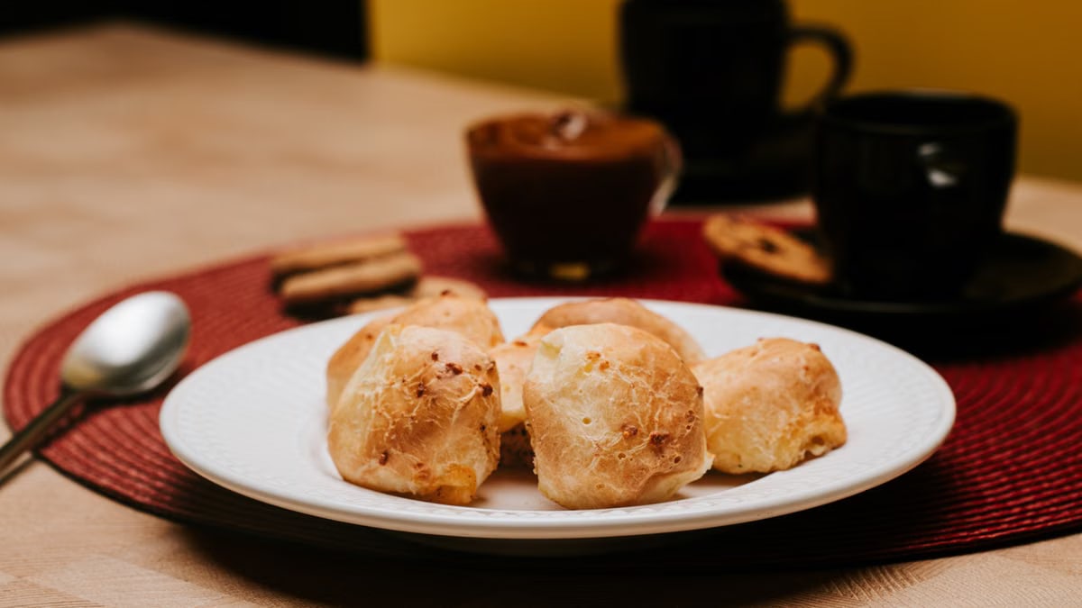 Tasty cheese bread rolls on a plate with coffee cups, creating a cozy atmosphere.